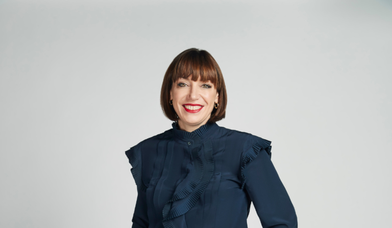 Beth Rigby stands in front of a white backdrop, smiling into the camera