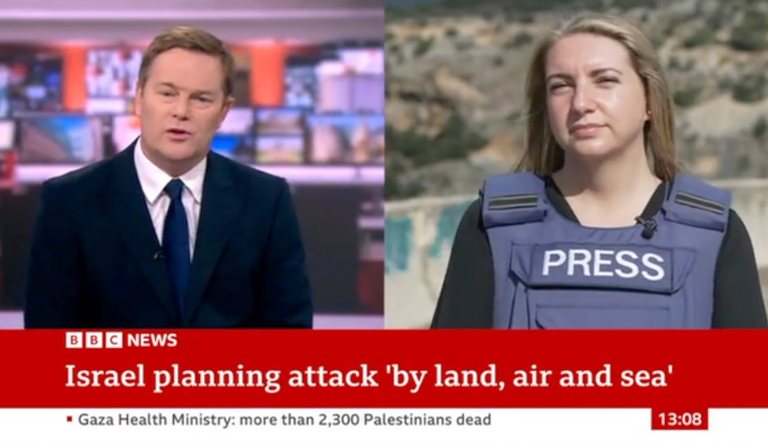 A news reporter in a studio talks to a second reporter, stood outside with a body armour vest labelled 'Press'. Part of the news chyron reads "Israel planning to attack 'by land, air and sea'"