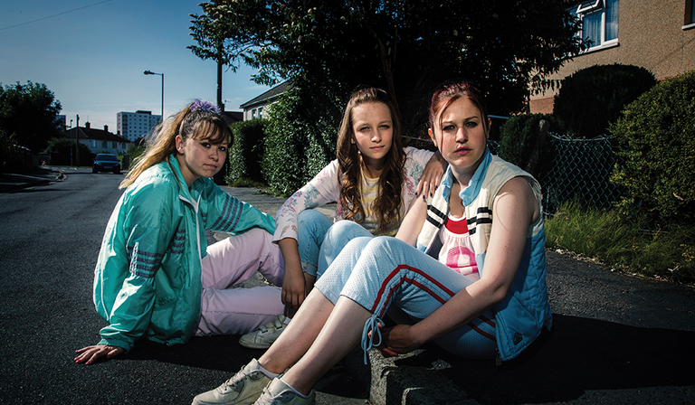 The cast of Three Girls sit on a curb