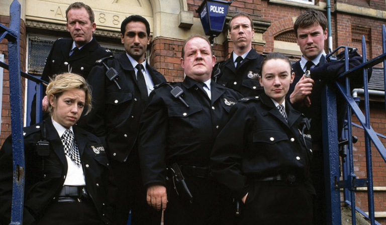 The cast of The Cops look into the camera, wearing police uniform and looking serious