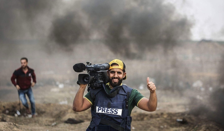Fadi Shana gives a thumbs up to the camera, wearing a body armour vest labelled 'Press'