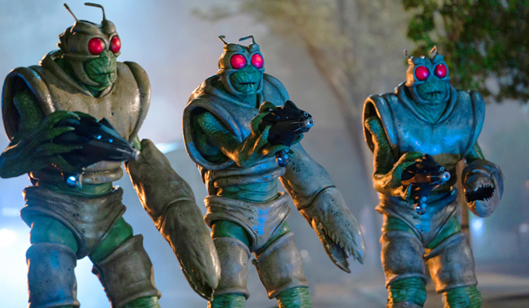 Three green Wrarth Warriors stand in the street, pointing guns at something off-camera