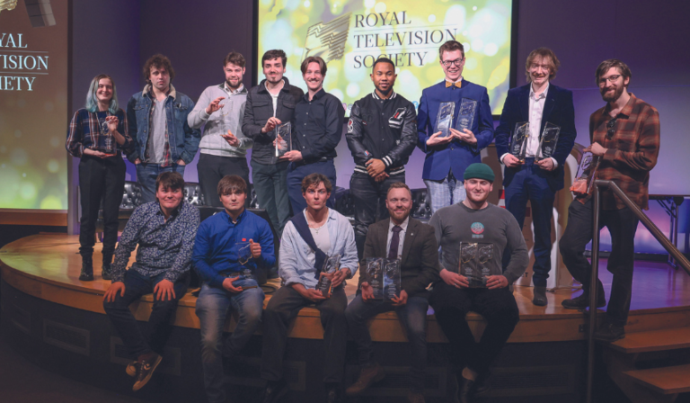 A group of students hold up RTS Awards in front of screens displaying the RTS branding