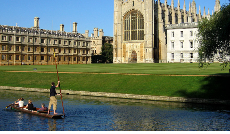 A man punts down a river in front of a church in Cambridge