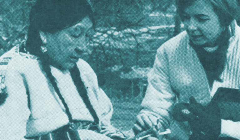A Native American woman sits next to another woman, talking. The image has a blue filter