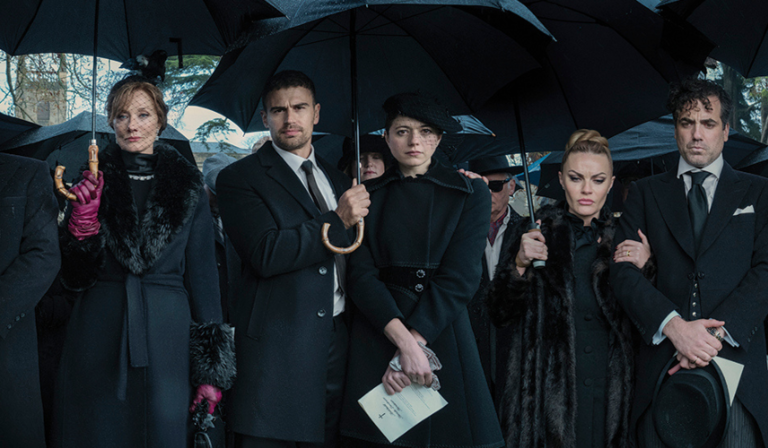A group of people stand in black tie formalwear holding umbrellas, looking sombre