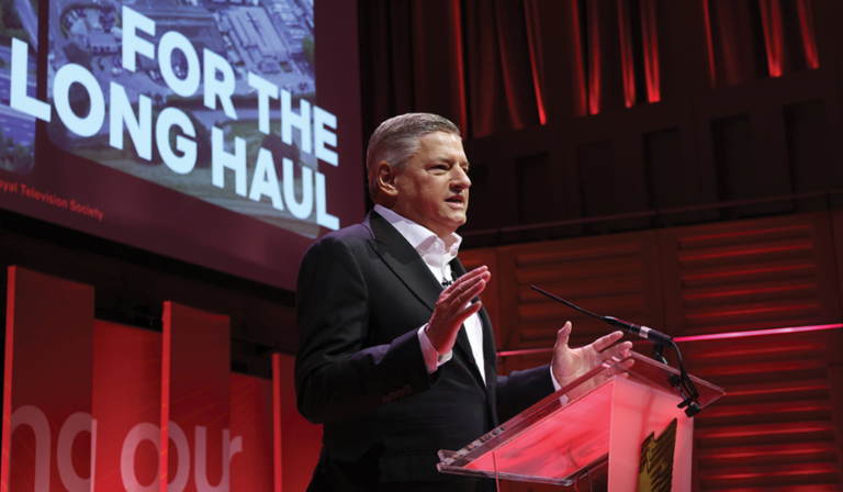 Ted Sarandos stands at a podium, delivering a talk at the RTS London Convention, beneath a screen on which text reading "FOR THE LONG HAUL" is visible