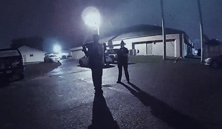 Figures stand outside in the dark, as seen through a grainy surveillance camera