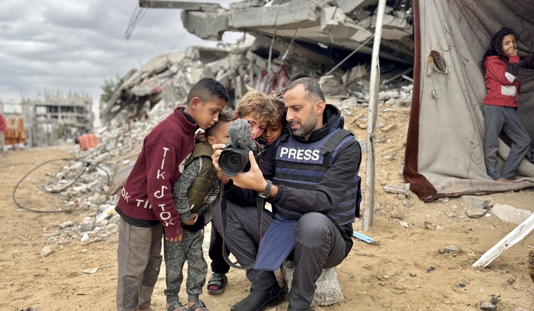 Mohammed shows footage on his camera to four children, standing amidst rubble