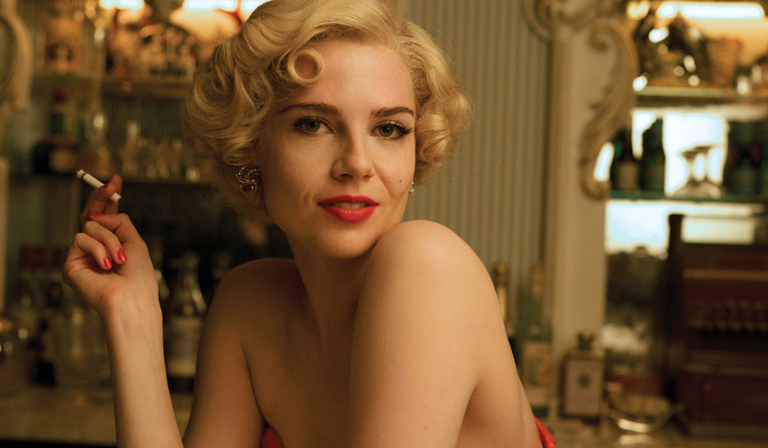 A white woman in her 30s with blonde hair wears a red dress and smokes a cigarette in an old pub