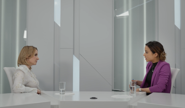 Two people sit across from each other in a white room, sat around the same white table
