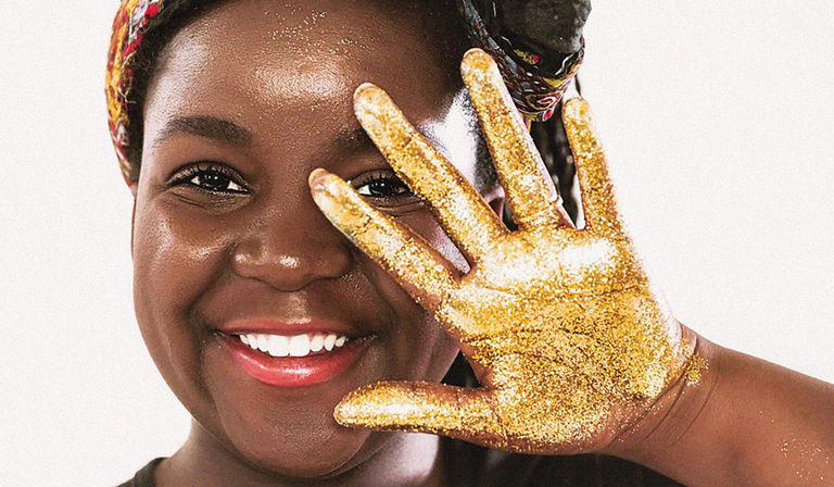 A smiling woman holds her hand out in a wave, covered in gold glitter