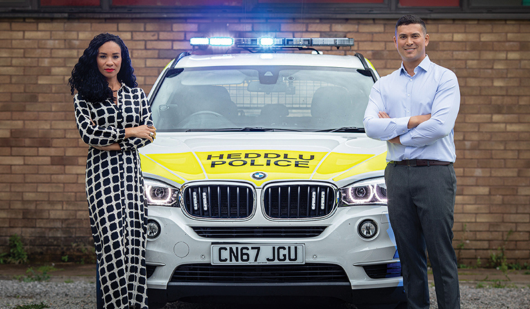 Michelle Ackerley and Rav Wilding fold their arms in front of a police car with its emergency lights on