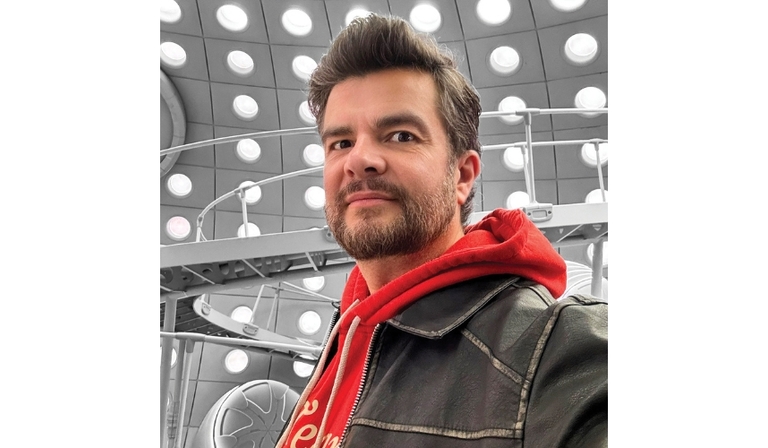 A selfie of a white man with grey-brown hair, wearing a red hoodie underneath a black leather jacket, as he stands in the newly revamped Doctor Who TARDIS