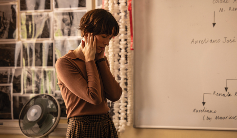 Rebecca Hall stands in a classroom, hands on her face and eyes closed, as if in pain