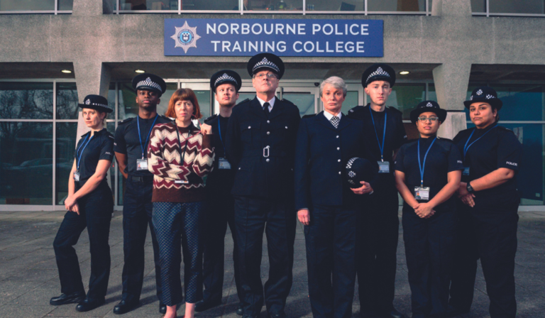 A group of police officers and trainees, one in plain clothes, stands outside Norbourne Police Training College