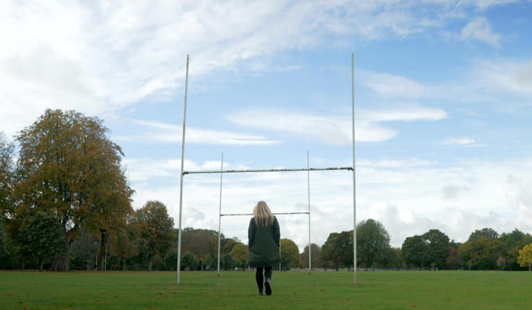 A woman walks down an otherwise empty rugby pitch