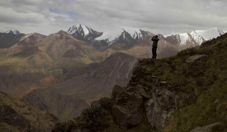 A man with binoculars stands on a mountain range